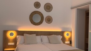 A bedroom with a wooden headboard, two wall-mounted lights, and three circular wall decorations. - MYO Barcelona Hotel & Apartments (Castelldefels)