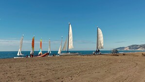 A beach with several sailboats anchored in the sand, a clear blue sky, and a distant coastline. - MYO Barcelona Hotel & Apartments (Castelldefels)