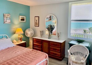 A bedroom with a bed, dresser, mirror, fan, and chair.