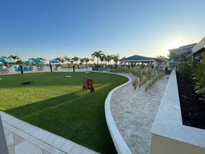 A landscaped outdoor area with a curved pathway, green lawn, and palm trees. - Sunset & Ocean Front Views-FM-Beach(Pool is Open) (Fort Myers Beach)