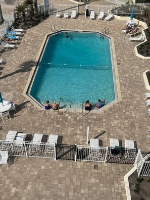 A rectangular swimming pool with a tiled deck surrounding it, equipped with lounge chairs and umbrellas. - Sunset & Ocean Front Views-FM-Beach(Pool is Open) (Fort Myers Beach)