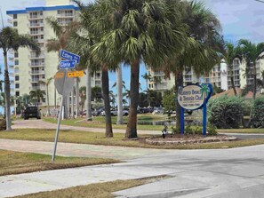 A street sign indicating 'Estero Blvd' and 'Gloria St' with a 'NO OUTLET' sign below. There's a sign for 'Estero Beach & Tennis Club' with a phone number. Palm trees and a building are in the background.