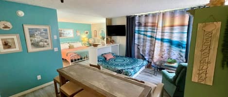 A compact living space with a dining area, a bed with a patterned bedspread, a green sofa, and a television.