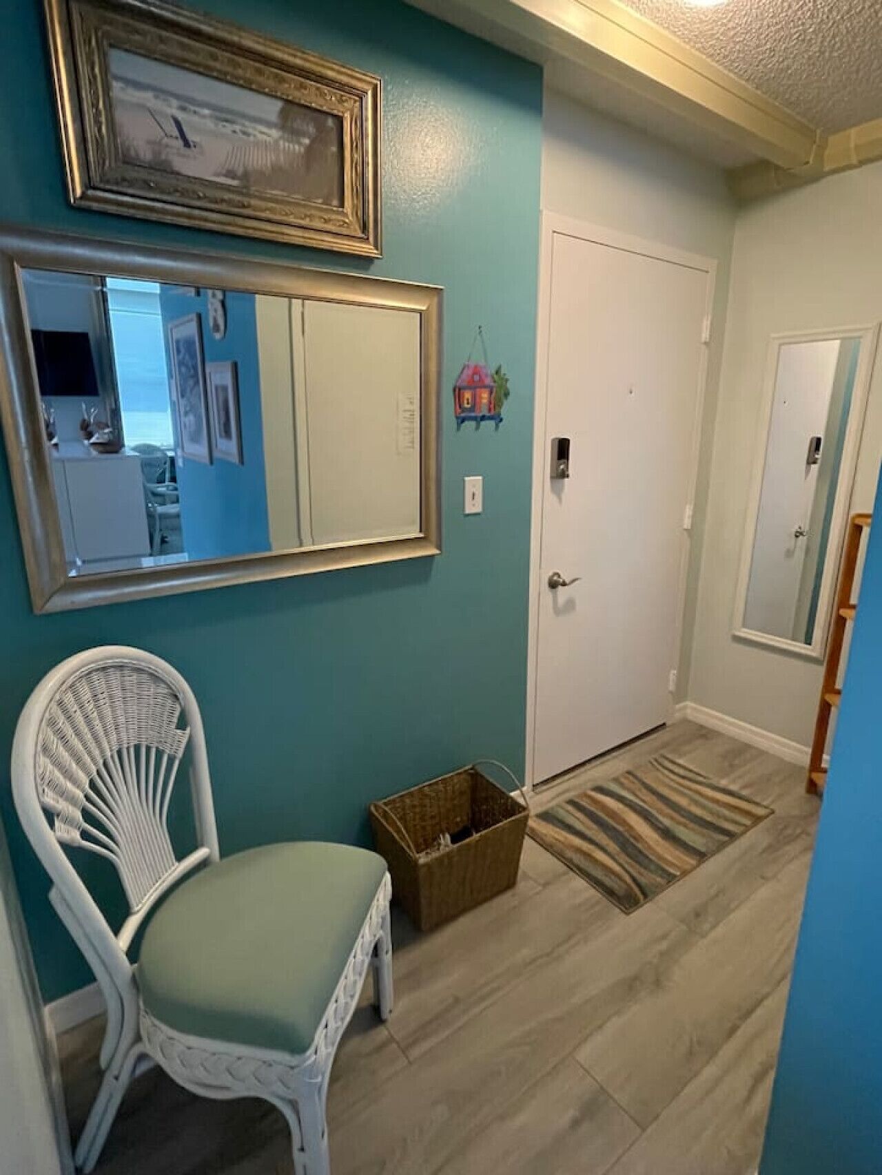 Un couloir aux murs de couleur turquoise, une chaise en osier blanche, un panier en bois et un tapis à rayures.