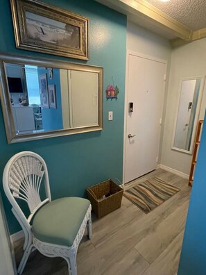 A hallway with teal walls, a white wicker chair, a wooden basket, and a striped rug.
