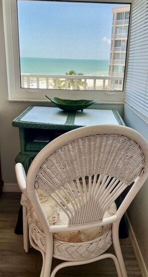 A wicker chair with a view of the ocean through a window.