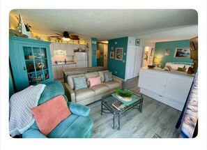 A living room with teal walls, a beige sofa, a glass coffee table, and a white cabinet. - Sunset & Ocean Front Views-FM-Beach(Pool is Open) (Fort Myers Beach)