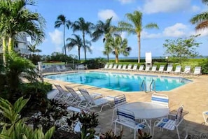 Ein Swimmingpool mit Liegestühlen und einem Tisch, umgeben von Palmen und blauem Himmel.