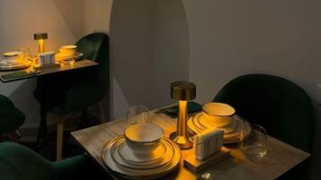 A dining area with a table set for two, featuring a modern lamp, plates, and cutlery.