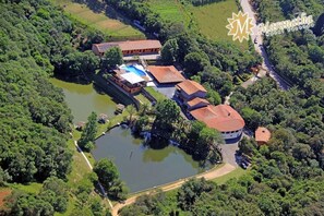 Une vue aérienne d’un hôtel doté d’une piscine, entouré d’une végétation luxuriante et d’un petit lac.