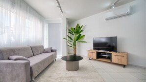 Un salon moderne avec un canapé, une table basse, un téléviseur posé sur un meuble en bois et une plante en pot.