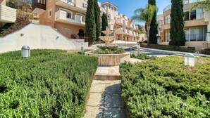Un quartier résidentiel avec des immeubles d’appartements modernes, une fontaine centrale et des espaces verts bien entretenus le long d’un sentier.