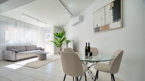 Un salon moderne avec une table à manger en verre, deux fauteuils beige, un canapé gris et une grande plante en pot.