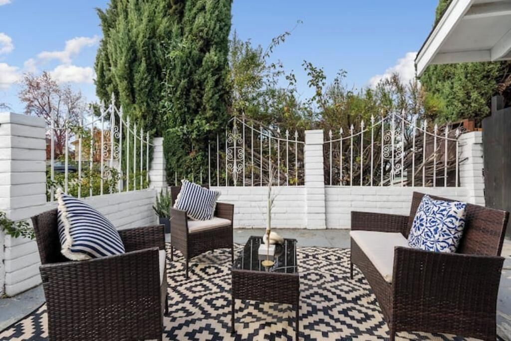 Eine Terrassenanlage im Freien mit Korbmöbeln, einem gemusterten Teppich und einem Zierzaun.