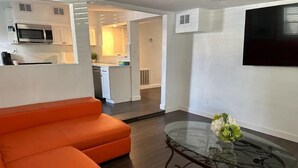 Ein modernes Wohnzimmer mit einem großen, orangefarbenen Ecksofa, einem Glastisch mit einer Vase und einem an der Wand montierten Flachbildfernseher.
