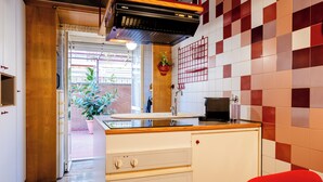 Une cuisine avec un plan de travail en bois, des armoires blanches, un four encastré et une chaise rouge.