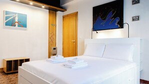 Une chambre d’hôtel avec un lit bien fait, une porte en bois, un téléviseur fixé au mur et une petite étagère.