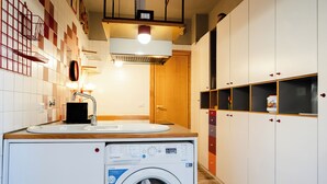 Une petite buanderie équipée d’un lave-linge, d’un évier et d’armoires en bois.
