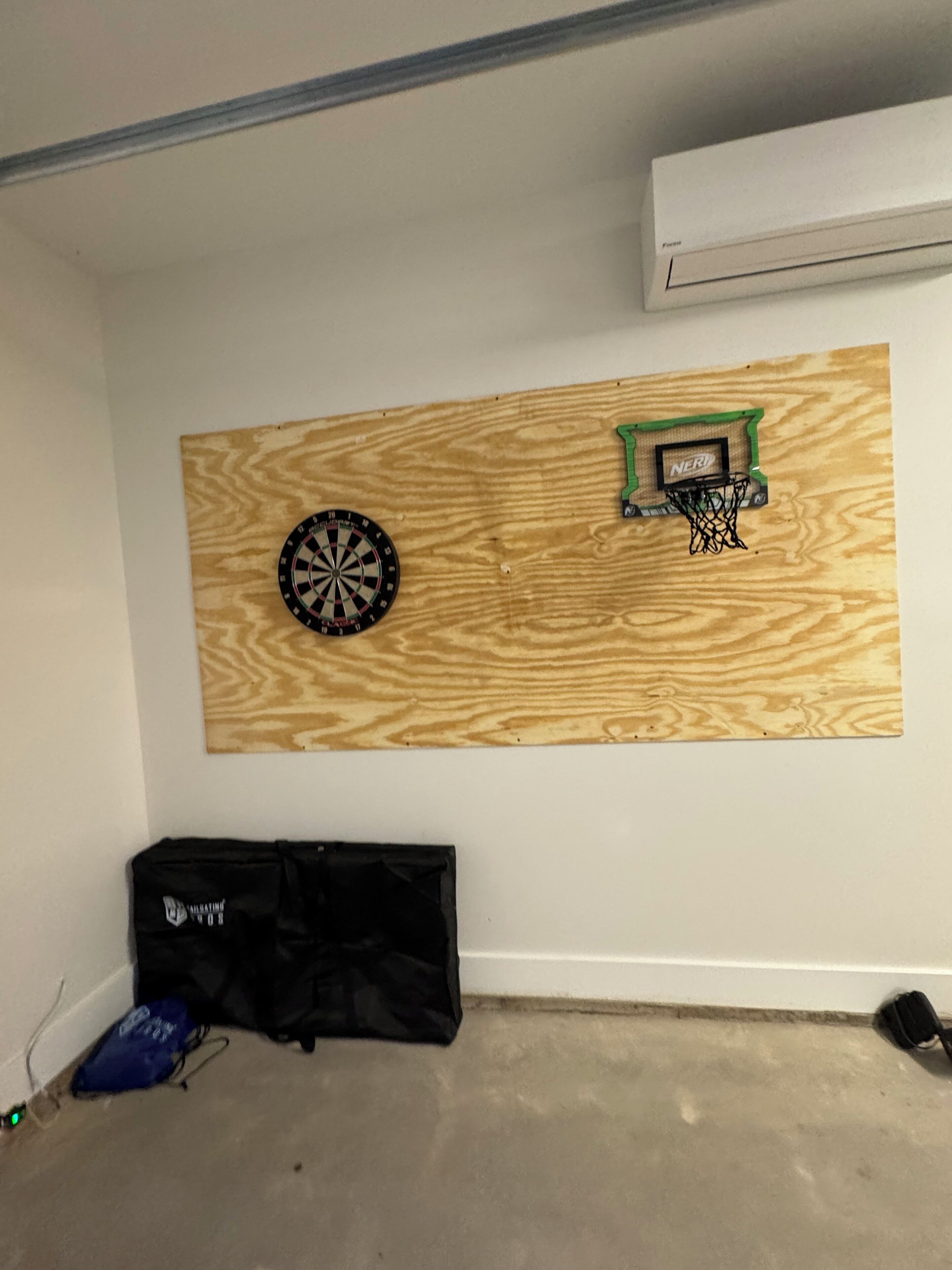 A room with a dartboard, a small basketball hoop, and a black bag on the floor.