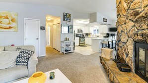 Een moderne woonkamer met een open haard, een keuken op de achtergrond en een accentmuur van steen.