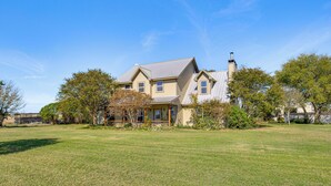 A two-story house with a front porch, surrounded by a well-maintained lawn and trees. - 30 Mi to Fort Worth: Rural Retreat w/ Patio! (Godley)