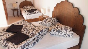 A bedroom with a wooden headboard, two beds with matching patterned bedding, a bedside table with a lamp, and a small round table with a lamp.