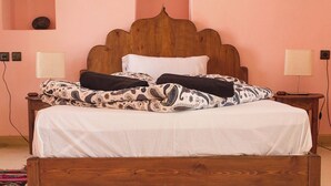 A wooden bed with a white sheet and patterned blankets, a wooden headboard, and a small bedside table with a lamp.