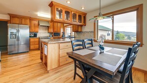 A kitchen with wooden cabinets, a stainless steel refrigerator, a dining table with chairs, and a window with a view. - Vineyard Farmhouse in Oakland w/ Hot Tub! (Oakland)