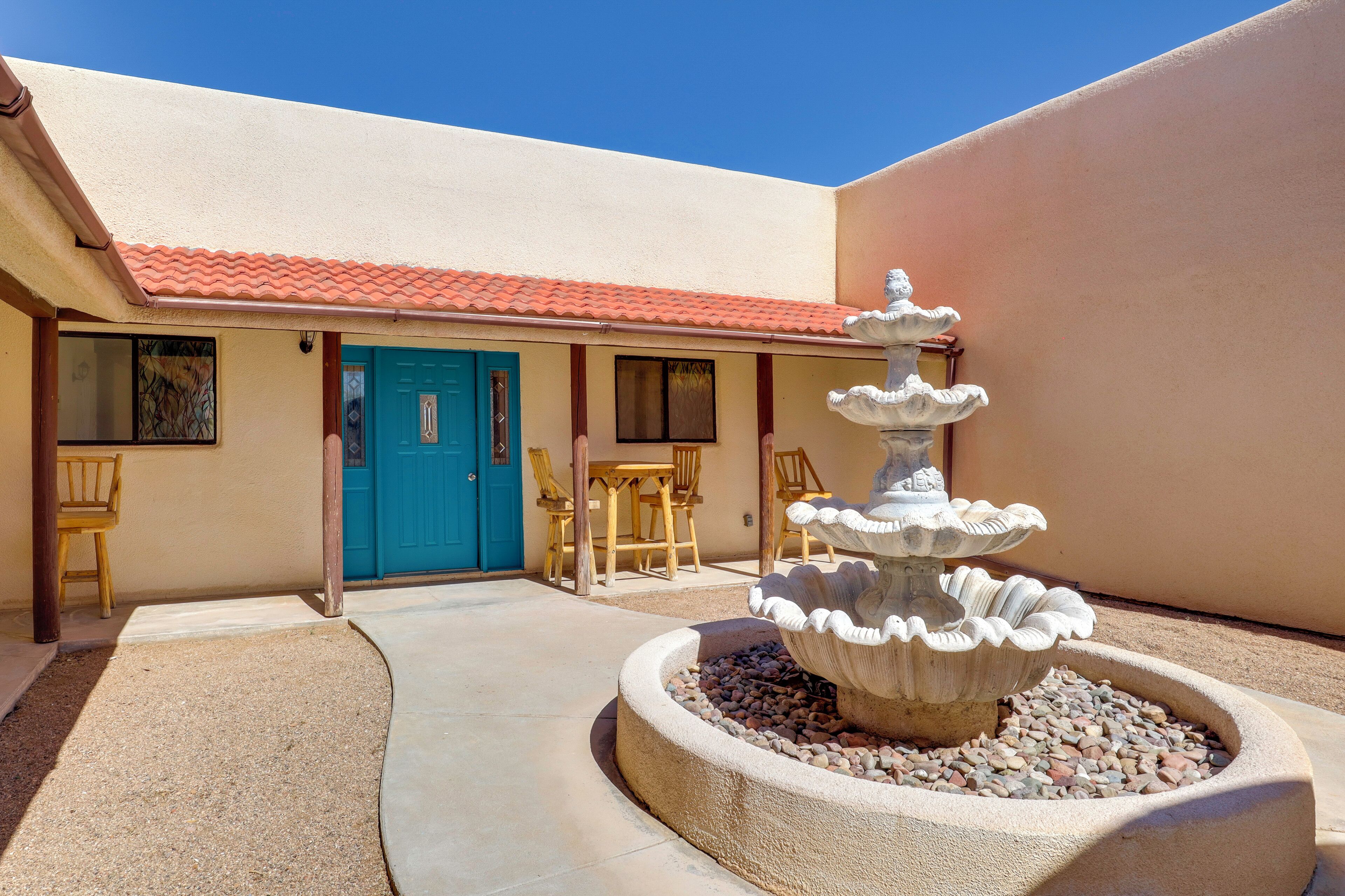A courtyard with a fountain, a blue door, and wooden furniture.