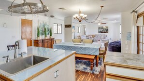 Uma cozinha moderna com uma ilha central, uma área de refeições com lustre e um espaço de estar com uma janela grande.