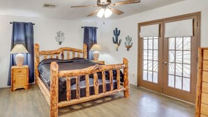 Quarto com cama de madeira, ventilador de teto, janela com persianas e porta com painéis de vidro.
