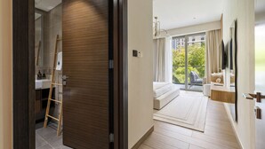 A modern hotel room with a wooden floor, a large sliding glass door leading to a balcony, a white sofa, and a wooden sideboard with a mirror. - Massive 1BR w/ Pool, Gym & Kid`s Play Area (Dubai)