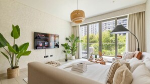 A modern hotel room with a large bed, a TV mounted on the wall, a window with a view of greenery, and a potted plant.