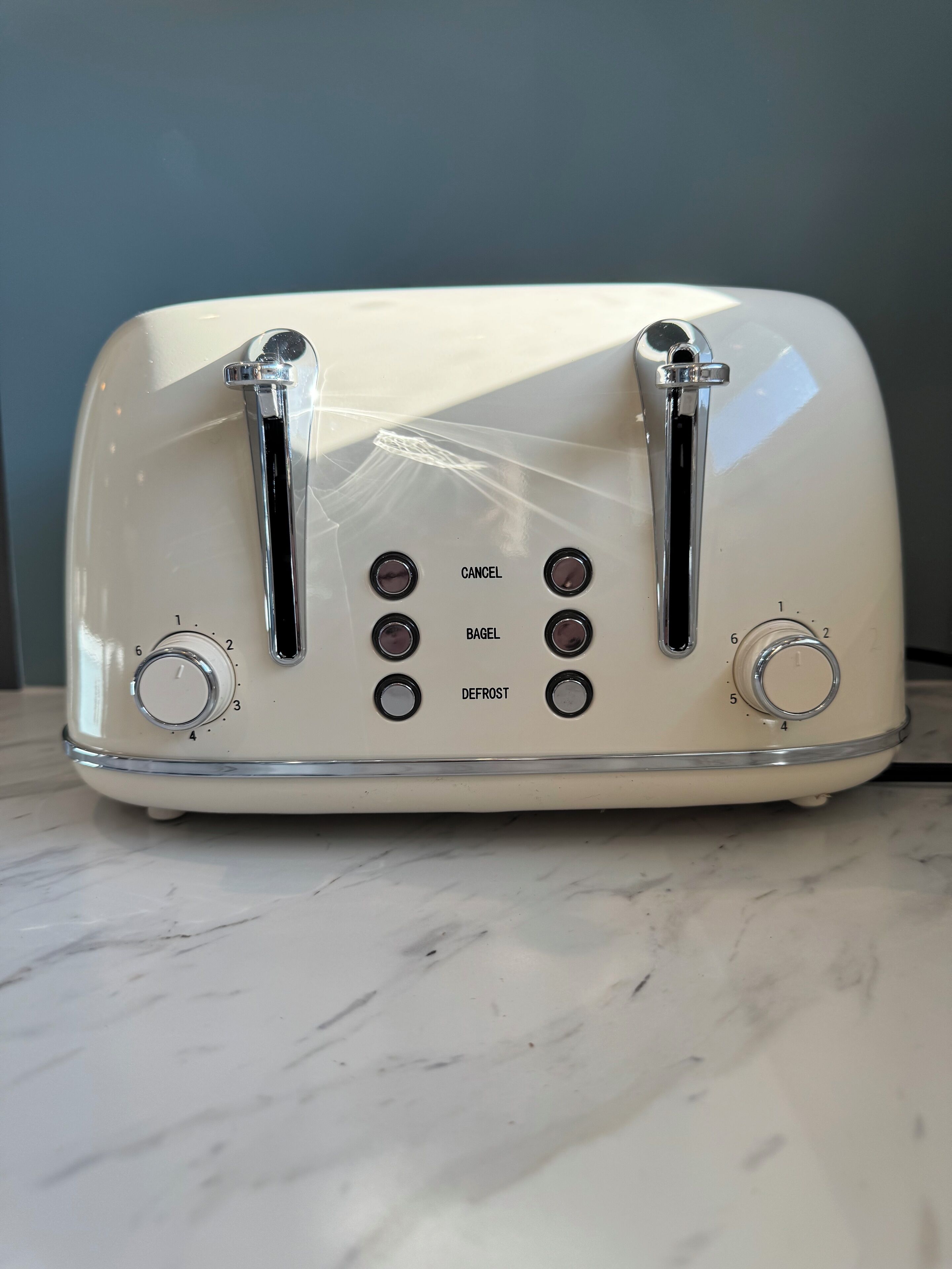 Un tostapane vintage bianco con quattro pulsanti etichettati ANNULLA, BAGEL e SCONGELARE, e due manopole.