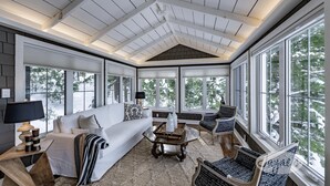 A spacious room with a high ceiling, large windows, a white sofa, a coffee table, and a patterned chair.