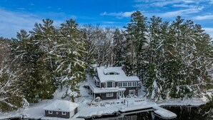 A large house surrounded by snow-covered trees and a lake.