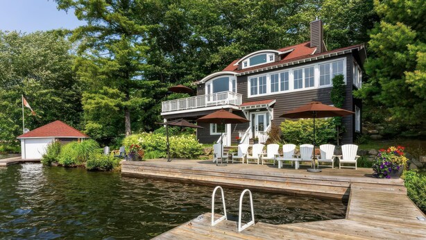 A house with a dock extending into a body of water, surrounded by lush greenery.