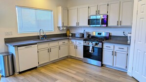 A modern kitchen with white cabinetry, stainless steel appliances, and a wooden floor. - 8 BEDROOM Fun Smart Stylish Home, 8 Minutes to the Strip (Las Vegas)
