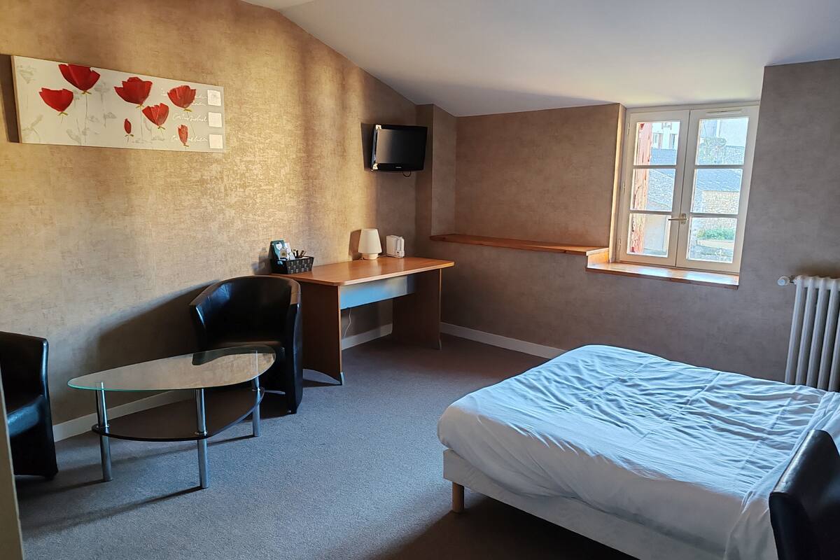 A bedroom with a bed, a desk, a chair, a TV, and a window.