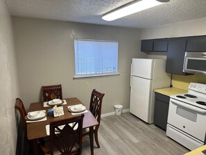 Cocina compacta con refrigerador, microondas y estufa. Hay una mesa de comedor dispuesta con platos y un ventanal encima.