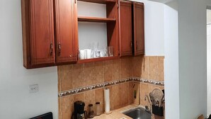 Une cuisine avec des meubles de rangement en bois, un plan de travail, un évier et une machine à café.
