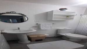 Une salle de bain avec un lavabo sur colonne, des toilettes, un miroir, un porte-serviettes et une petite étagère sur laquelle est posée une plante.