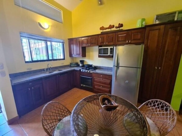 A compact kitchen with wooden cabinets, a stainless steel refrigerator, a microwave, and a gas stove.