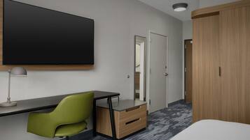 Une chambre d’hôtel moderne équipée d’un grand téléviseur à écran plat fixé au mur, d’un bureau avec une chaise, d’une armoire et d’un miroir.