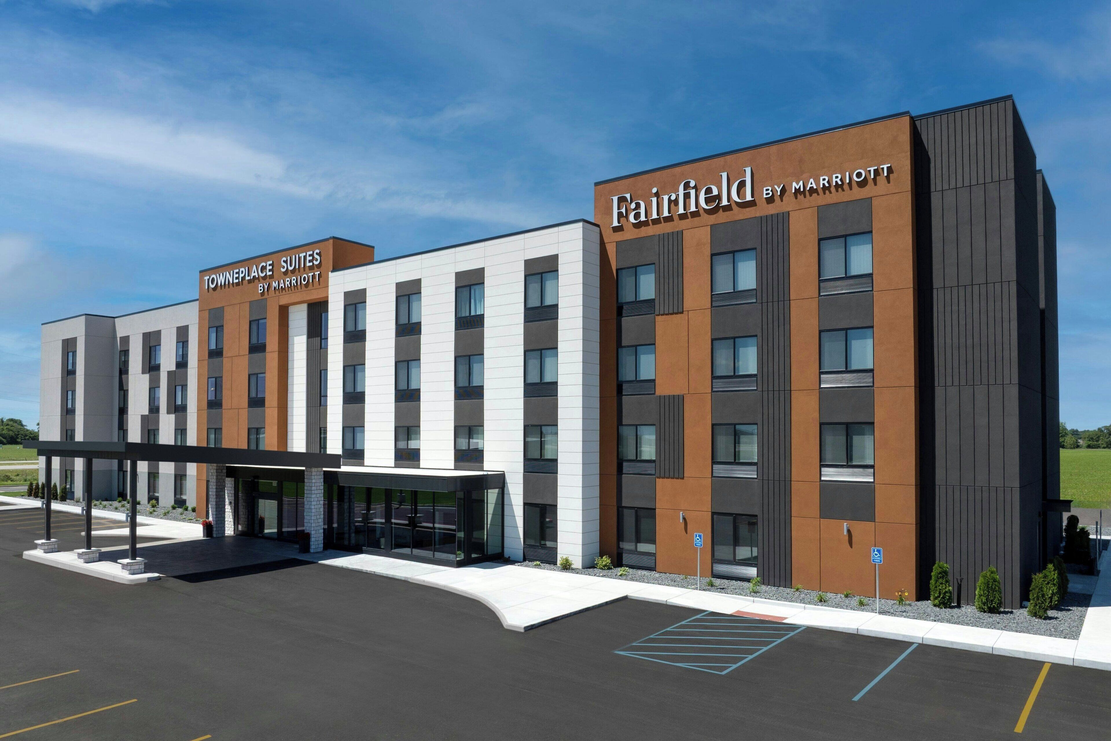 A modern hotel with a two-story structure, labeled "Fairfield by Marriott" and "Towneplace Suites by Marriott." It features a covered entrance and a parking lot with marked spaces.