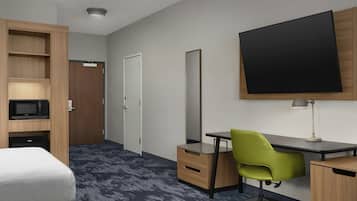 Habitació d'hotel amb escriptori, una cadira verda, televisió de pantalla plana, microones, armari i una porta.