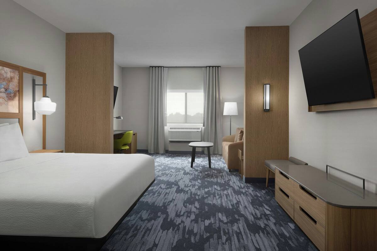 A hotel room with a large bed, a desk, a chair, a TV, and a window with curtains.