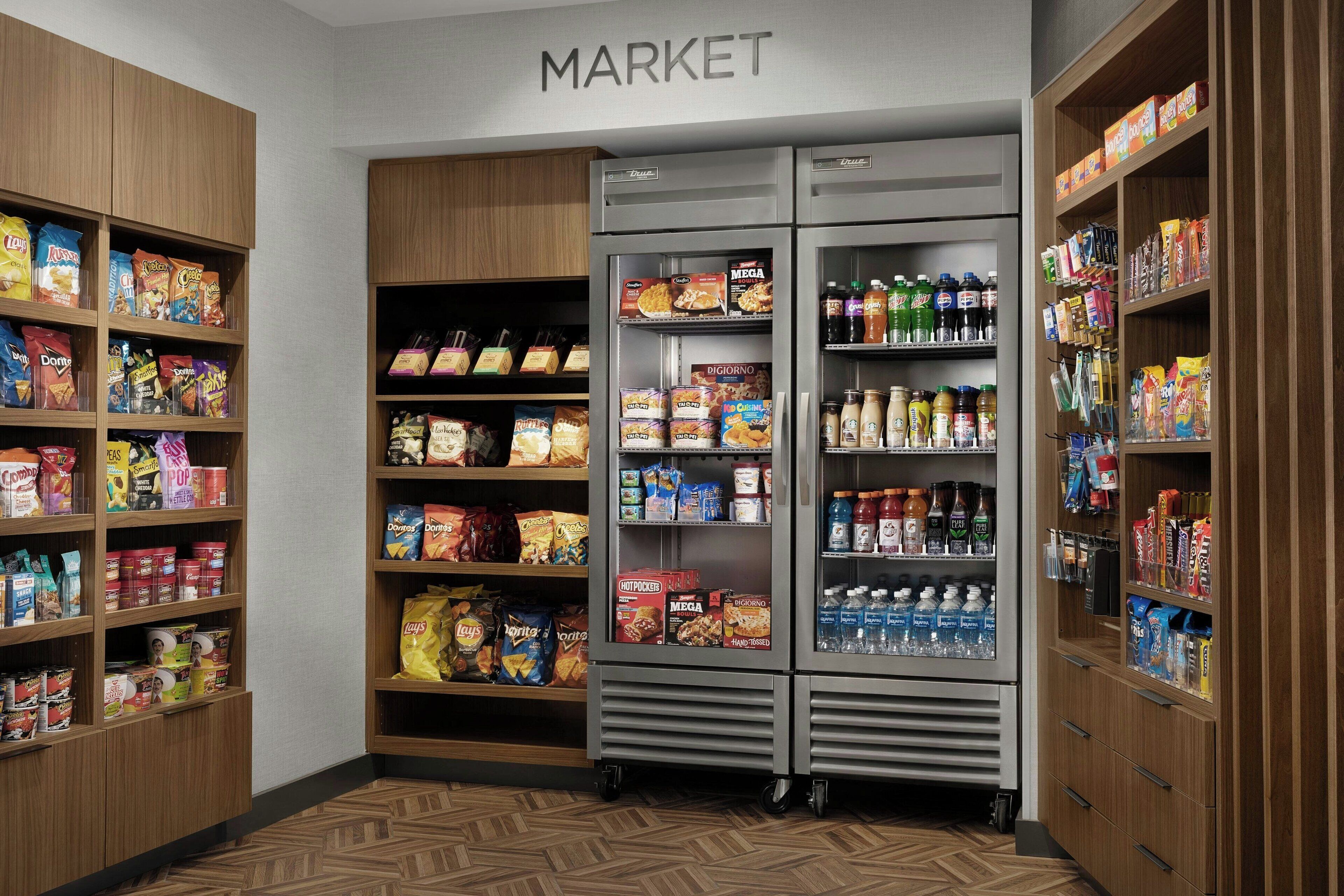 Zona de mercado con estantes llenos de aperitivos, bebidas y otros productos alimenticios.