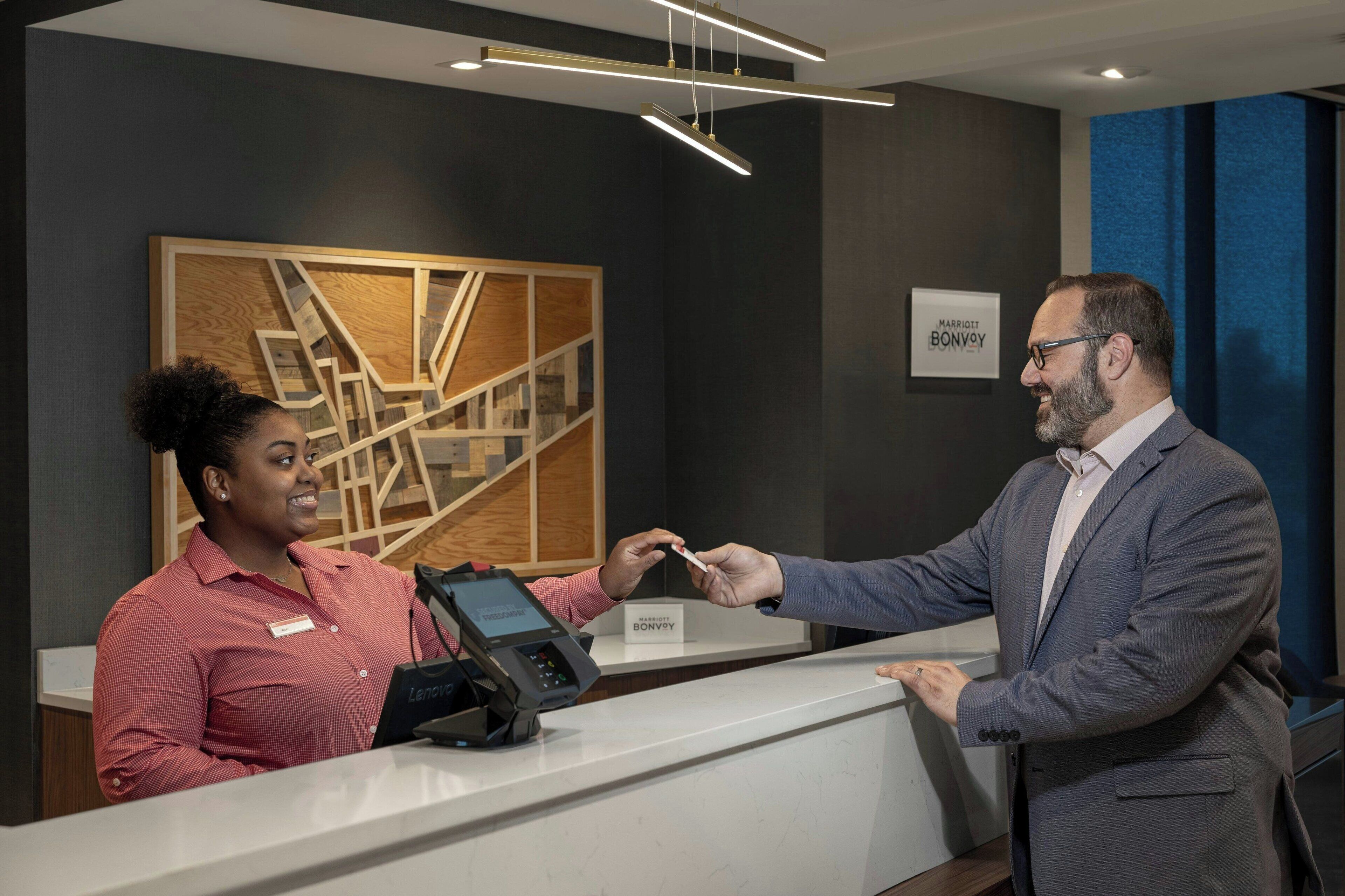 A hotel reception area with a modern design, including a reception desk, a digital payment terminal, and a sign for the Marriott Bonvoy hotel.