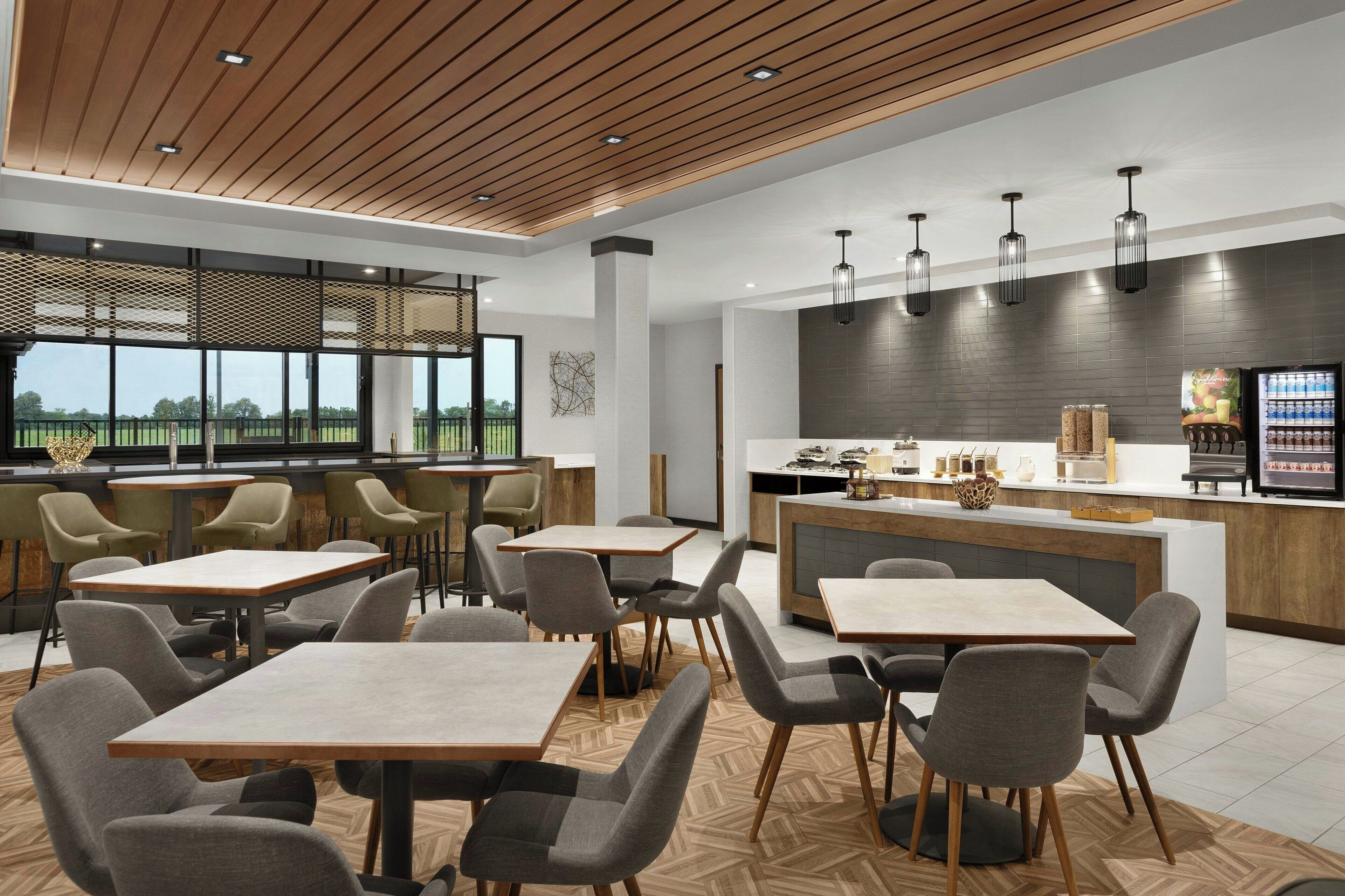 A modern restaurant with a wooden ceiling, large windows, and a central bar area.